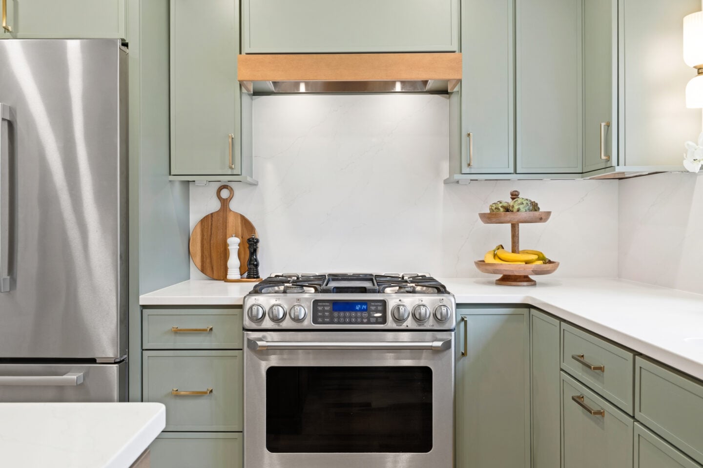 Decorative kitchen range hood with wood trim and soft green cabinetry