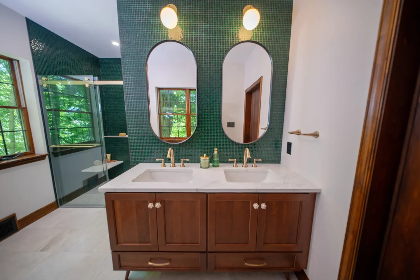 Double vanity with custom cherry cabinetry and dramatic bottle-green glass mosaic feature wall.