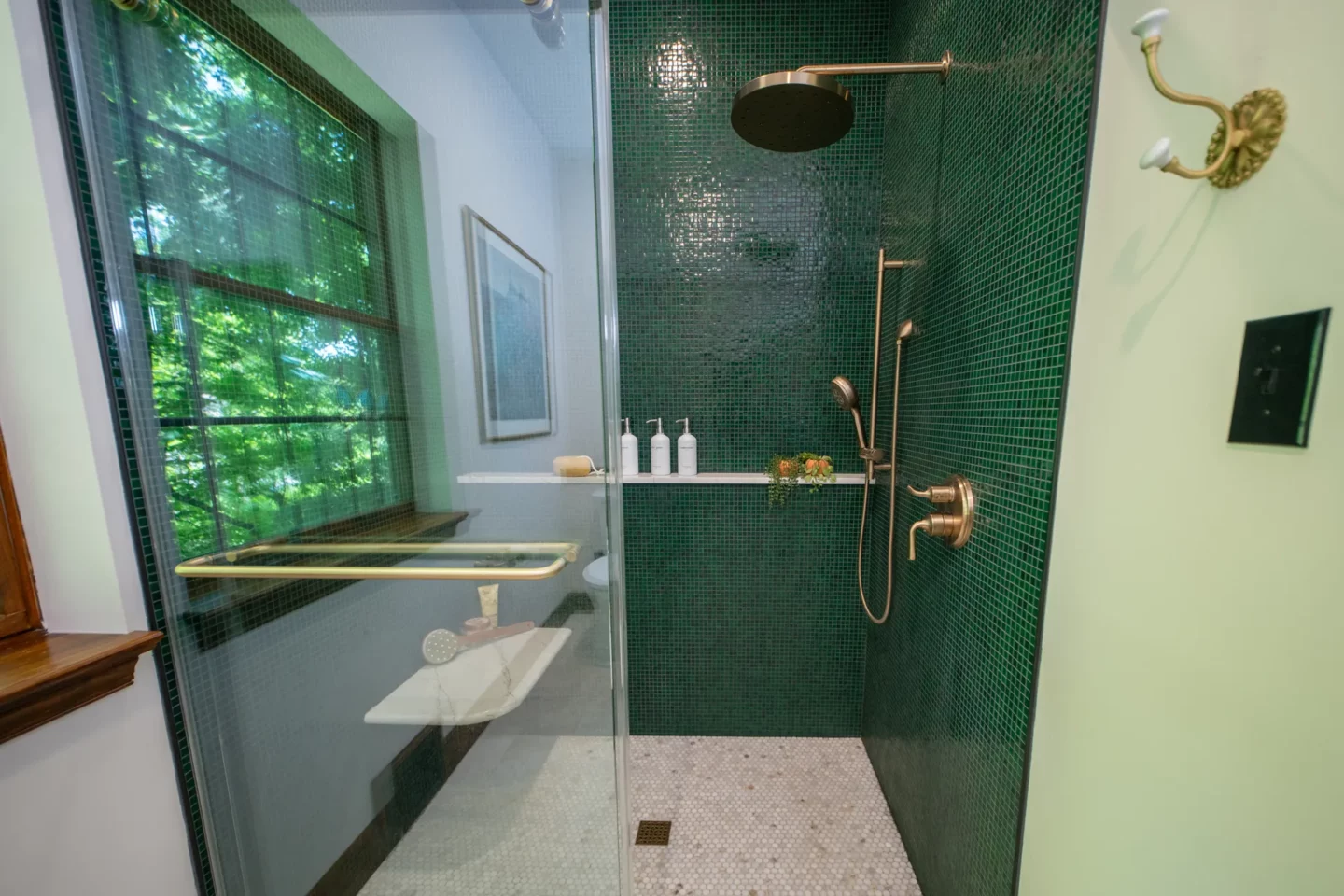 Walk-in shower featuring bottle-green glass mosaic tile and polished marble shower flooring.